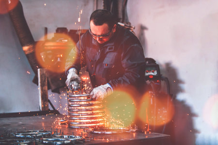 Locksmith in special clothes and goggles works in production. Metal processing with angle grinder. Sparks in metalworking.の写真素材