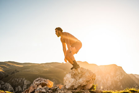 Man doing conditioning training on top of a mountain in the early morning with the sunrise in the...