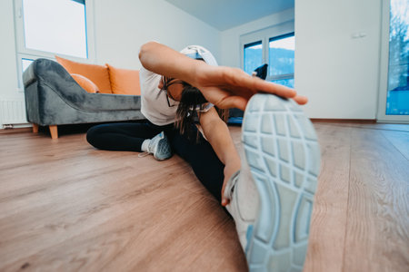 A woman stretching in her apartment during early morning after training , reflecting her dedication to a healthy lifestyle. This moment highlights the importance of regular exercise and self-care, even in the comfort of ones own homeの写真素材