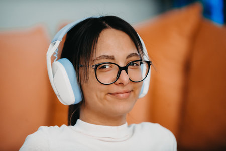 Young woman wearing glasses and headphones while training at home. Her active pose and determination showcase her commitment to a healthy lifestyle, with the modern interior serving as a backdrop for her indoor workout routine.の写真素材