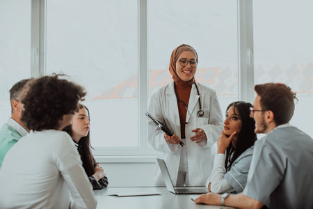 A group of multiethnic medical professionals including doctors, surgeons, and nurses are gathered in a hospital setting discussing patient care and using modern technology to address challenges in the medical field.の写真素材