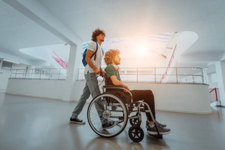 African American student pushing his friends wheelchair through a modern school, demonstrating inclusion, accessibility, and the power of friendship.Assistance to people with disabilitiesの写真素材