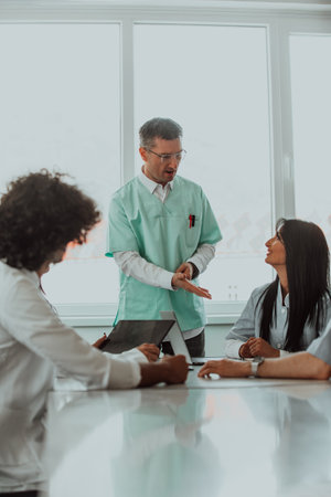 A group of multiethnic medical professionals including doctors, surgeons, and nurses are gathered in a hospital setting discussing patient care and using modern technology to address challenges in the medical field.の写真素材