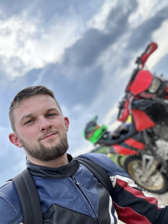 A professional motorcyclist resting on a forest road after an adventurous ride and taking a selfie...