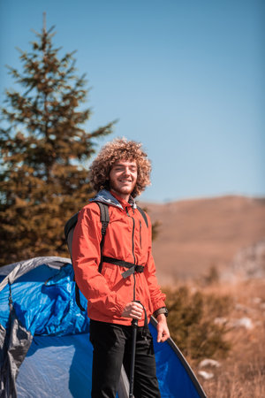 A man camping with a tent. He is surrounded by a beautiful mountain landscape, and the sun shines on his face, foreshadowing a beautiful and sunny day. The man looks satisfied and fulfilled, suggesting that he is enjoying his adventurous journey.の写真素材