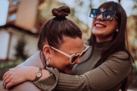 Two young women embrace each other emotionally outside on a sunny day while wearing sunglassesの写真素材