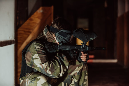 Photo of paintball player in goggle mask and camouflage aiming by paintball gun. Selective focusの写真素材