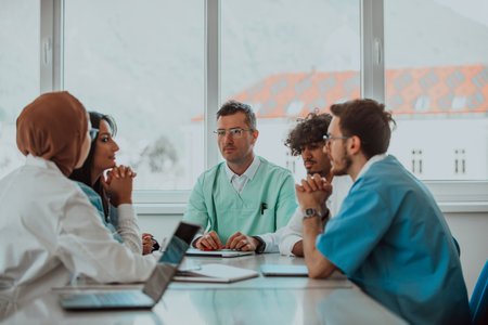A group of multiethnic medical professionals including doctors, surgeons, and nurses are gathered in a hospital setting discussing patient care and using modern technology to address challenges in the medical field.の写真素材