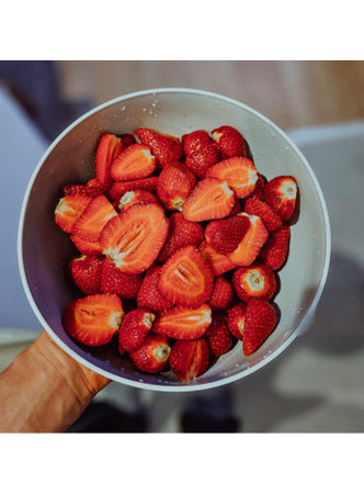 A man delicately holds a bowl filled with fresh, vibrant strawberries, showcasing their luscious red color and enticingly sweet aroma.の写真素材