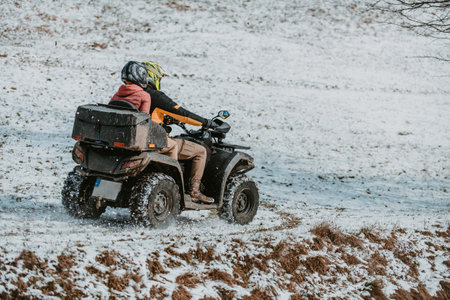 A young adventurous couple embraces the joy of love and thrill as they ride an ATV Quad through the snowy mountainous terrainの写真素材