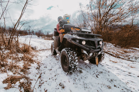 A young adventurous couple embraces the joy of love and thrill as they ride an ATV Quad through the snowy mountainous terrainの写真素材