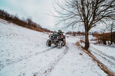 A young adventurous couple embraces the joy of love and thrill as they ride an ATV Quad through the snowy mountainous terrainの写真素材