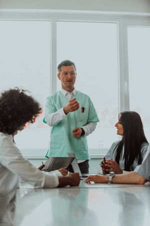 A group of multiethnic medical professionals including doctors, surgeons, and nurses are gathered in a hospital setting discussing patient care and using modern technology to address challenges in the medical field.の写真素材