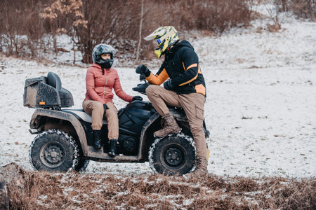 A young adventurous couple embraces the joy of love and thrill as they ride an ATV Quad through the snowy mountainous terrainの写真素材