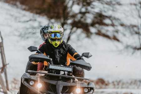 A young adventurous couple embraces the joy of love and thrill as they ride an ATV Quad through the snowy mountainous terrainの写真素材