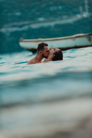A romantic young couple sharing a passionate kiss amidst the serene beauty of the ocean at sunset.の写真素材