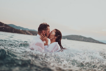 A romantic young couple sharing a passionate kiss amidst the serene beauty of the ocean at sunset.の写真素材