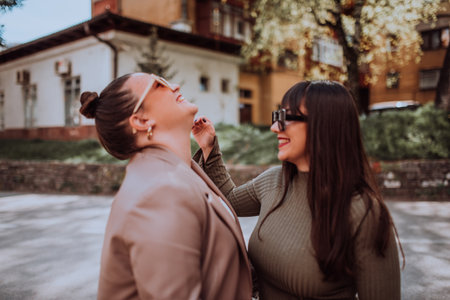 Two young women embrace each other emotionally outside on a sunny day while wearing sunglassesの写真素材