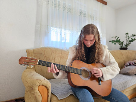 The young, curly-haired girl plays her acoustic guitar with passion and talent in the comfort of her...