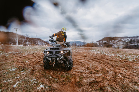 A man is fearlessly enjoying an adventurous ride on an ATV Quad through hazardous snowy terrain, embracing the thrill and excitement of the challenging mountainous landscapeの写真素材