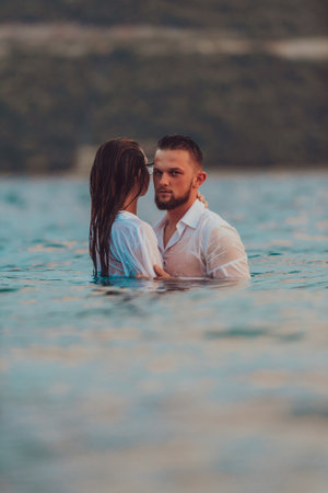 A symbolic and emotionally connected couple tenderly embraces against the backdrop of a serene sea, bathed in the warm hues of a breathtaking sunsetの写真素材