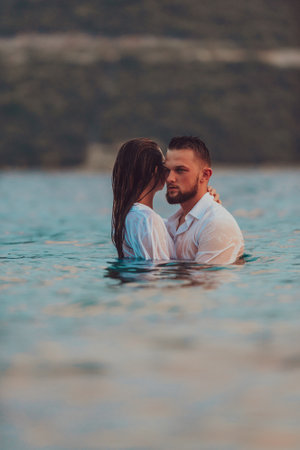 A symbolic and emotionally connected couple tenderly embraces against the backdrop of a serene sea, bathed in the warm hues of a breathtaking sunsetの写真素材