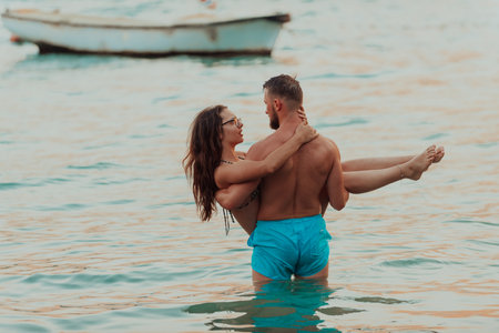 A handsome man tenderly holds his girlfriend in his arms while standing in the sea during the enchanting sunset, capturing a moment of muscular strength and affectionate romance against the backdrop of the ocean horizonの写真素材