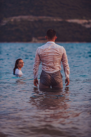 A romantic couple, adorned in white attire, stands in the sea, symbolically gazing at each other during the mesmerizing sunset, creating a serene and enchanting scene against the backdrop of the ocean horizonの写真素材