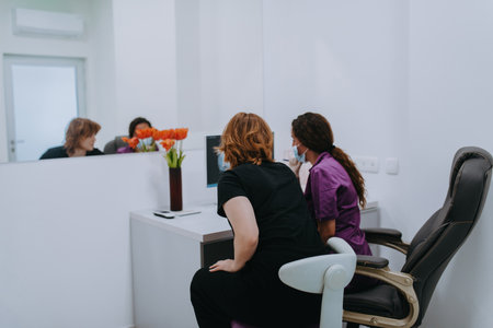 In a modern dental office, a dentist and a young patient engage in a collaborative consultation, exploring new tooth shades and discussing treatment options using a computerの写真素材