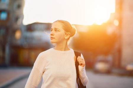 A beautiful blonde teenager returns home from school during the sunset, carrying her school...