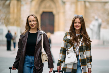 Two female tourists explore a European city, pulling their suitcases along as they wander through the charming streets, immersing themselves in the culture and beauty of their travel destinationの写真素材
