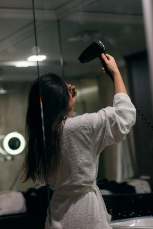 A joyful woman, with headphones in her ears, playfully dries her hair with a hairdryer in the...