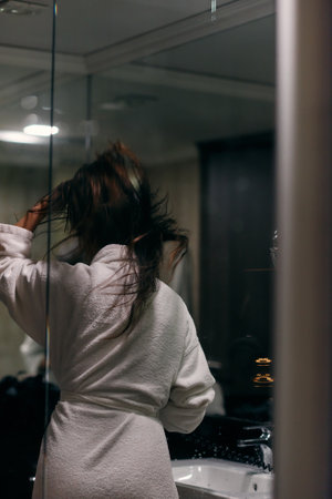 A joyful woman, with headphones in her ears, playfully dries her hair with a hairdryer in the bathroom after a refreshing bath, embodying a carefree and energetic moment of self-care and relaxationの写真素材
