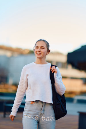 A beautiful blonde teenager returns home from school during the sunset, carrying her school backpack, in a serene and peaceful urban settingの写真素材