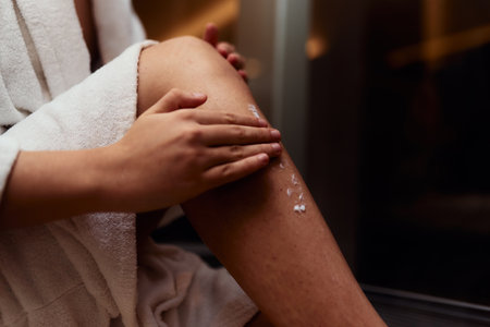 A woman indulges in her self care routine, pampering her skin after a relaxing bath by applying hydrating cream to her legs, embracing the essence of beauty and well beingの写真素材