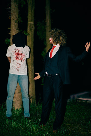 In the ominous stillness, a disguised person in a suit with wild hair stands beside another person, exuding an aura of tension and mystery.の写真素材