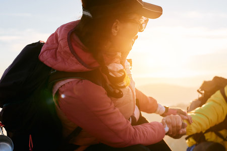 A hiker helps a friend climb the mountain at sunrise.A man in a yellow jacket extends a helping hand to his companion while climbing a rocky mountainの写真素材