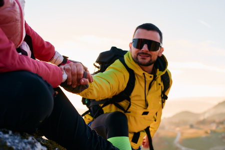 A hiker helps a friend climb the mountain at sunrise.A man in a yellow jacket extends a helping hand to his companion while climbing a rocky mountainの写真素材