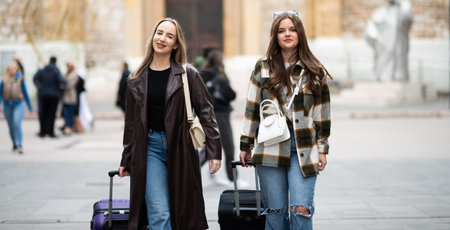 Two stylish young women walking outdoors with suitcases, exploring an urban destination during travel.の写真素材