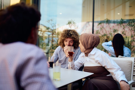 A European man with an Afro American hairstyle enjoys a drink with his Muslim friend in a cozy outdoor cafe.の写真素材