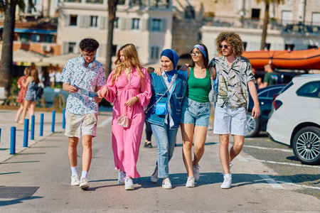 A diverse group of tourists, dressed in summer attire, strolls through the tourist city with wide...
