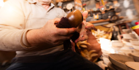 A senior man sitting in the workshop and smearsing wooden utensils with linseed oilの写真素材