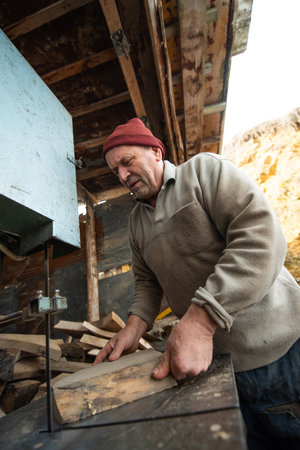 Carpenter Cutting Wood with a Bandsaw in a Rustic Workshopの写真素材