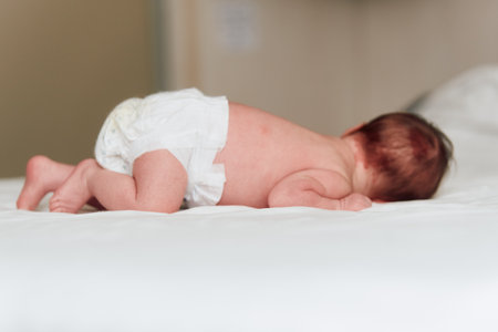 Rear view of a newborn baby wearing a diaper and lying on a white bed surface.