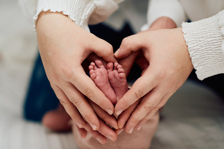 A close up of parents hands forming a heart around their newborns tiny feet, symbolizing love, family, and new beginnings.の写真素材