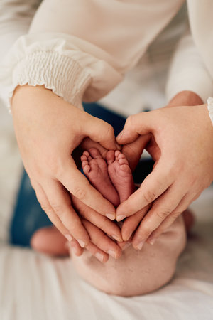A close up of parents hands forming a heart around their newborns tiny feet, symbolizing love,...