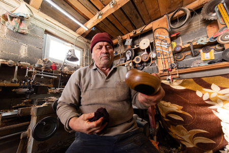 A senior man sitting in the workshop and smearing wooden utensils with oil