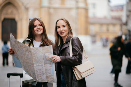 Two female tourists standing with luggage while reading a map and planning their route in the city.