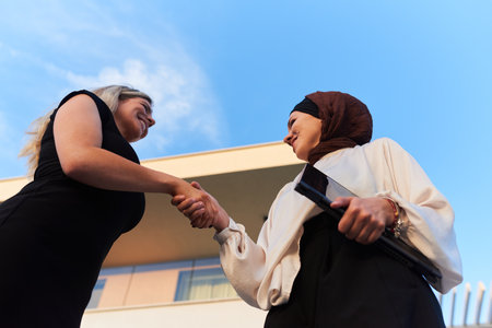 In a real-life scene, a Muslim woman in a hijab, who is a real estate business owner, shakes hands with a blonde woman after successfully selling a propertyの写真素材