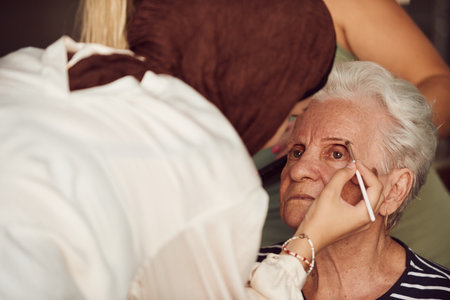 In this heartwarming real-life scene, a girl in a hijab and her sister lovingly apply makeup to their elderly grandmother, preparing her for a special family anniversary celebration, showcasing the bonds of family and cultural traditionsの写真素材